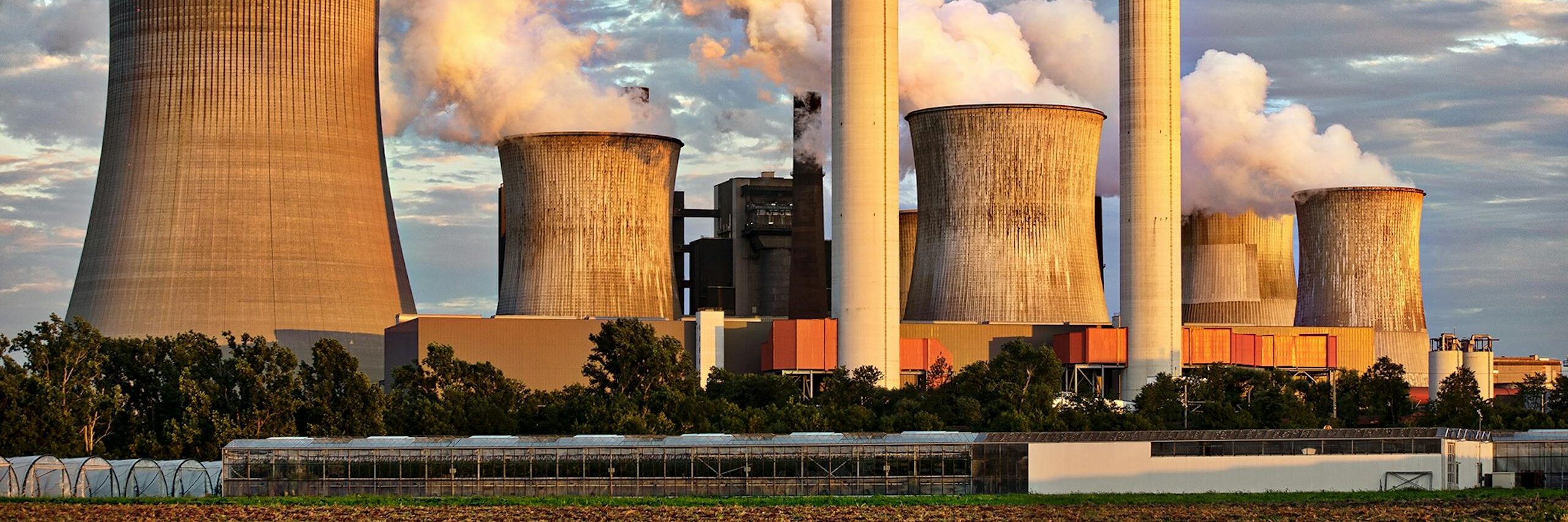 View of a power plant with smoke emissions under a cloudy sky, depicting industrial energy production.